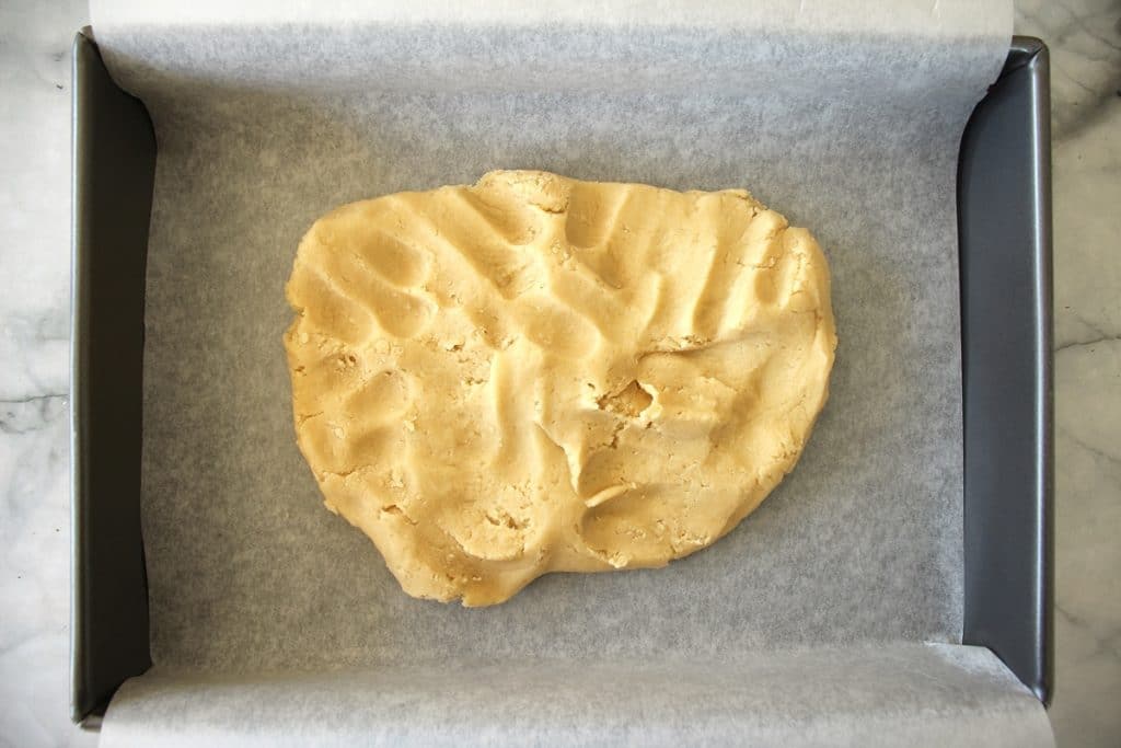 Dough in the midst of being pressed into a baking pan