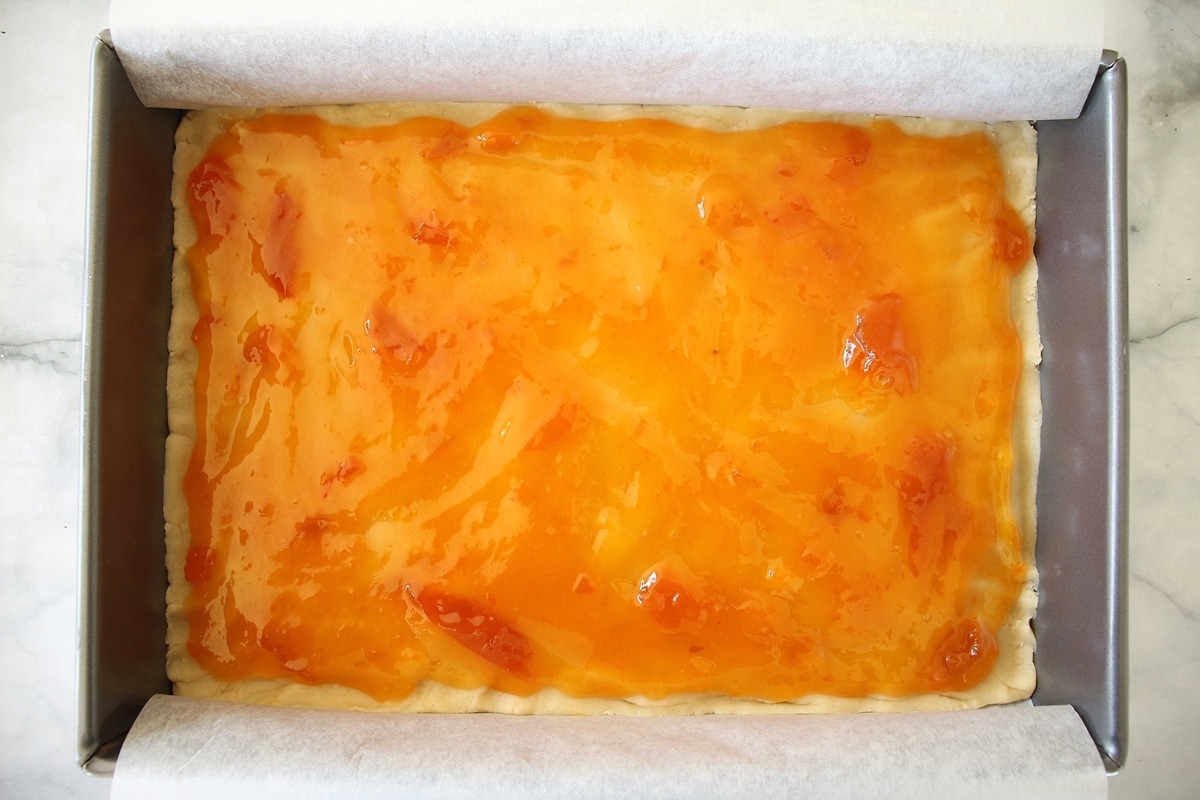 Dough pressed in a baking pan topped with apricot preserves