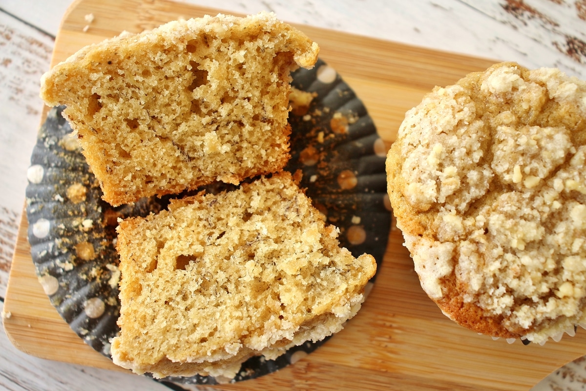 Two banana muffins on a small wooden board, with one cut in half