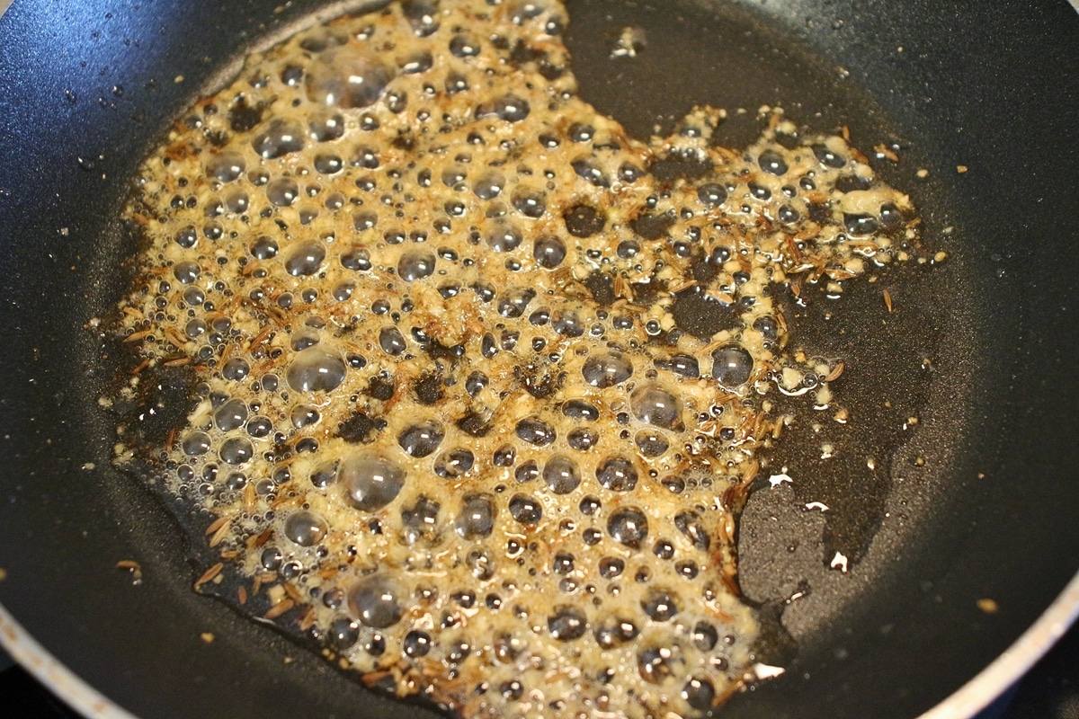 A small non-stick skillet with fried cumin seeds, garlic, and chili powder.