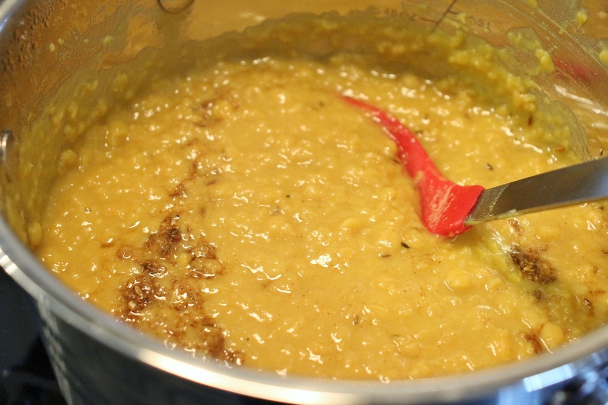 A pot of chana dal (bengal gram) being with a red silicone spoon.