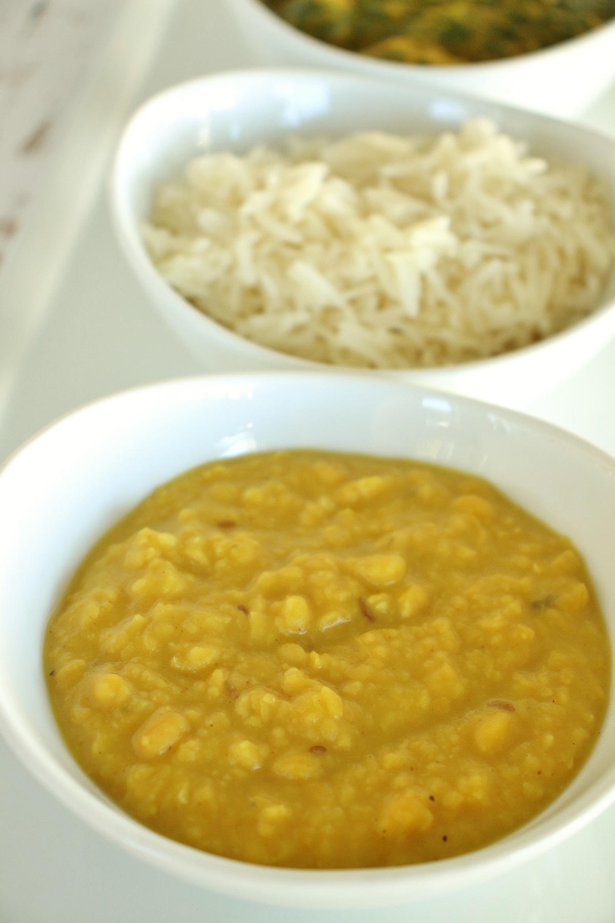 Bowls of chana dal, basmati rice, and another green curry lined up in a row.