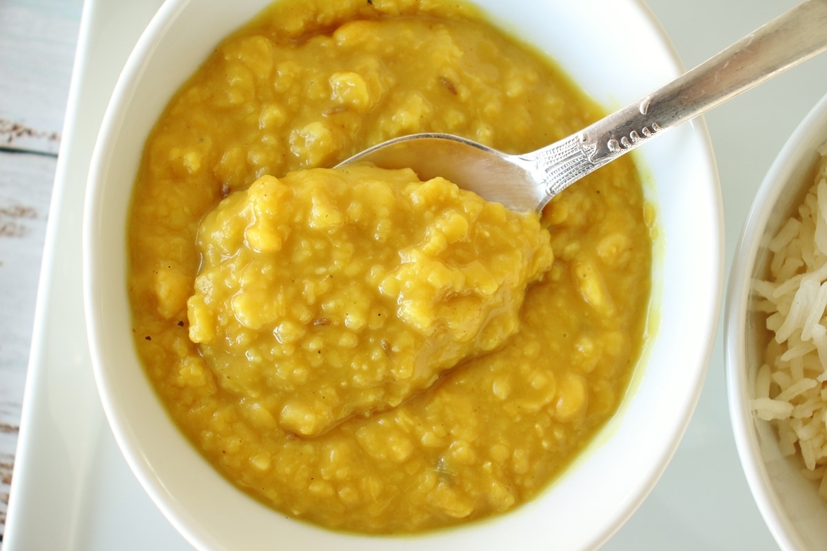 A bowl of yellow chana dal curry with a spoon lifting some out.