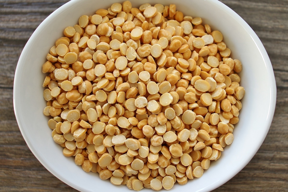 Uncooked chana dal (bengal gram) in a white bowl on a wooden surface.