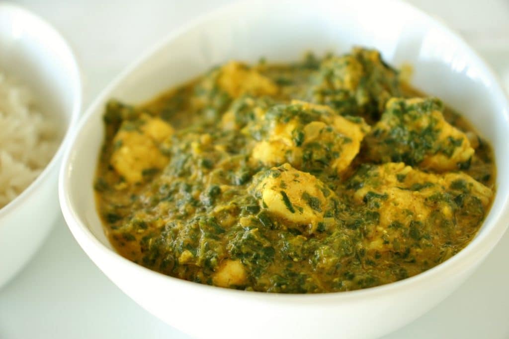 Indian chicken saag spinach curry in a white bowl with a bowl of basmati rice to the side