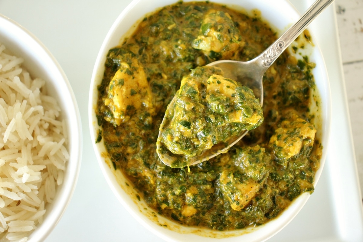 Indian chicken saag spinach curry in a white bowl with a spoon lifting some out