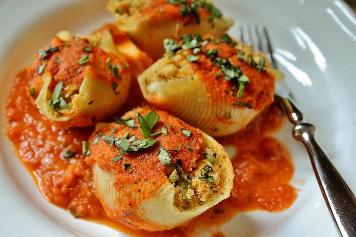 four stuffed pasta shells on white plate with folk on one side