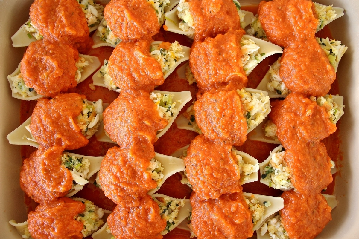 Crab stuffed shells arranged in a rectangular casserole dish topped with tomato sauce