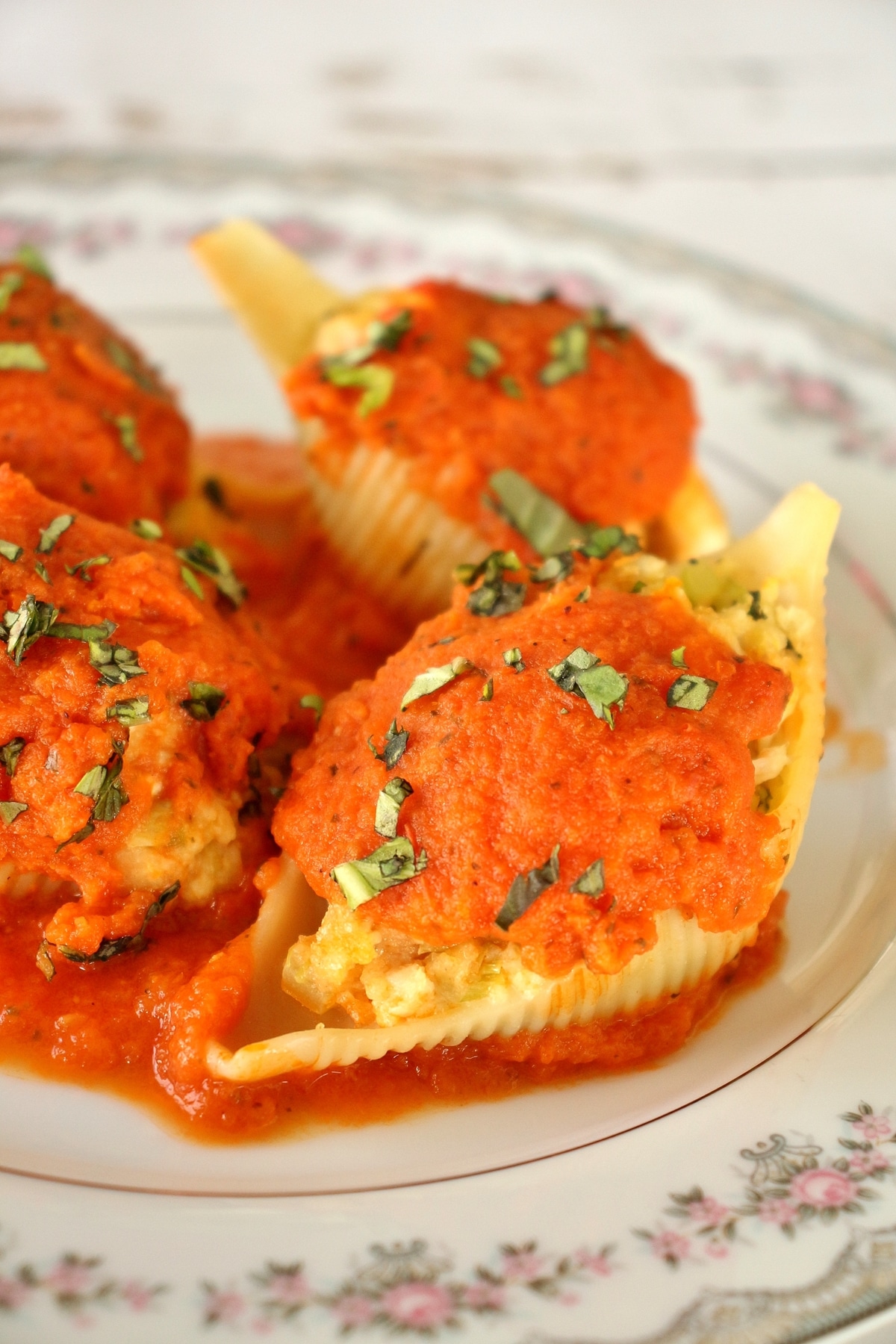 stuffed shells with tomato sauce and basil on fine china plate