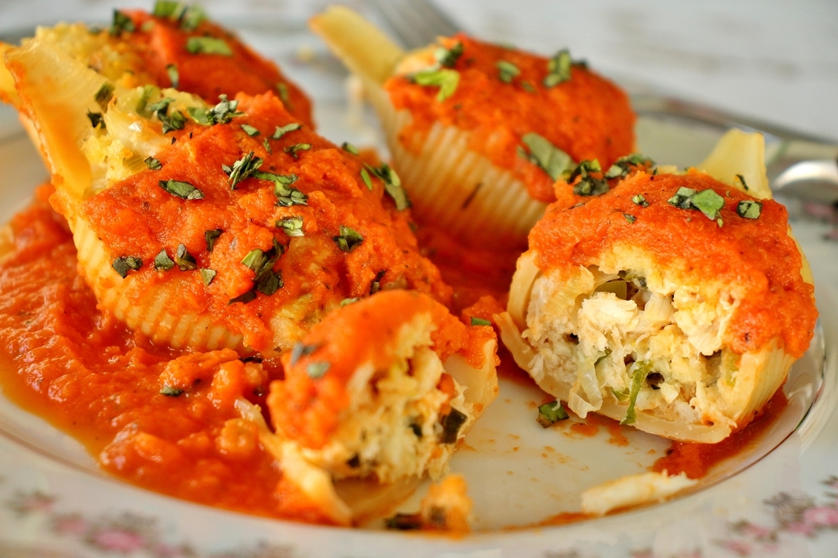 Four crab stuffed shells on fine china. One shell is cut to show the filling inside.