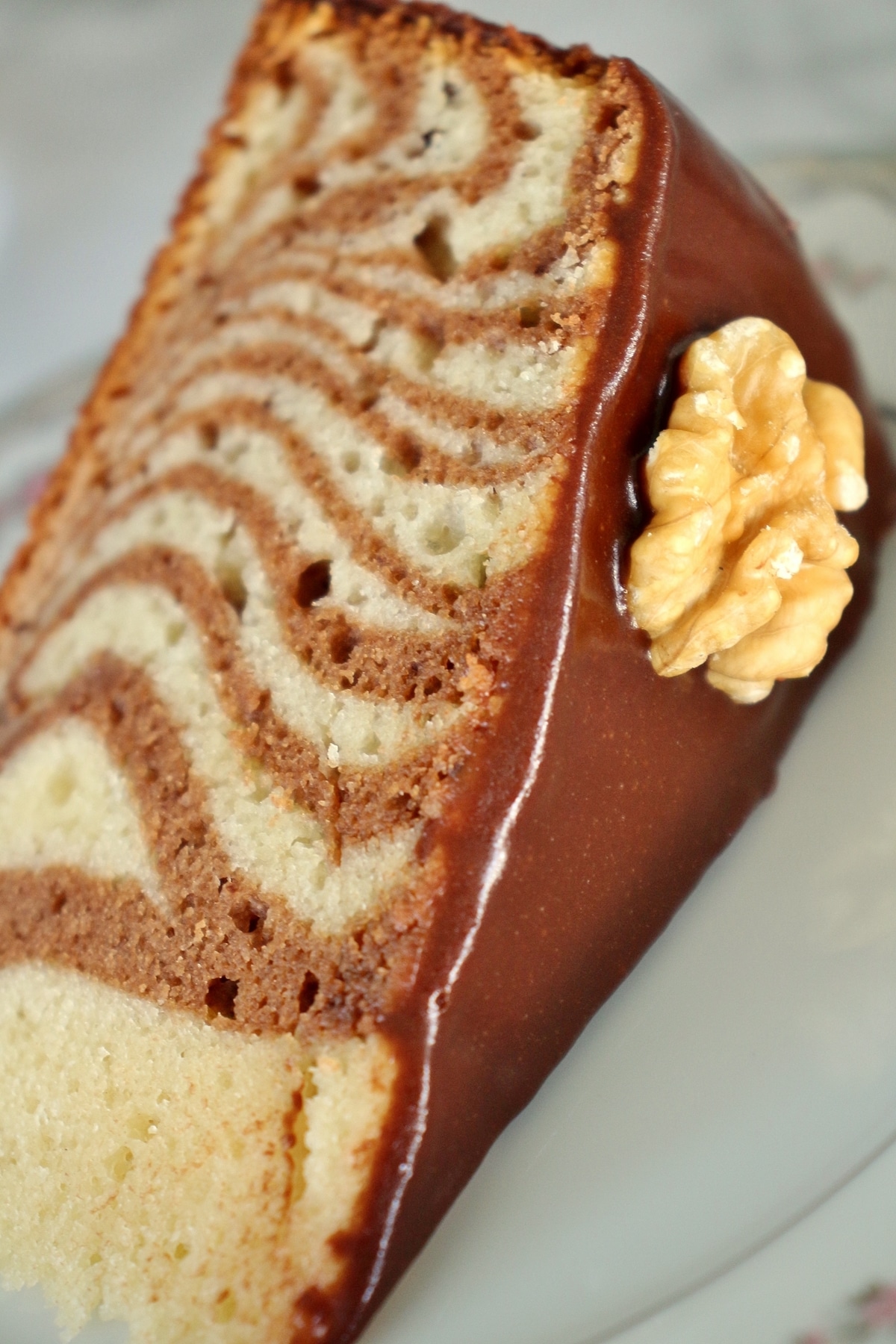 Close up of a slice of zebra cake with chocolate glaze and a walnut garnish
