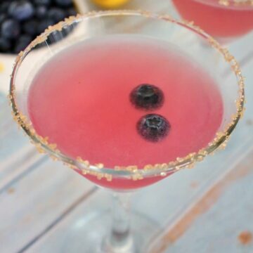 2 blueberry lemon drop martinis with a bowl of blueberries and fresh lemon in the background