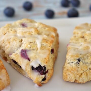 3 blueberry lemon scones on a rectangular white plate with spilled blueberries on the table