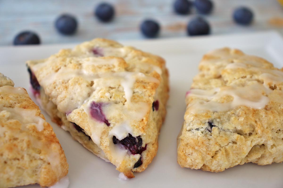 3 blueberry lemon scones on a rectangular white plate with spilled blueberries on the table