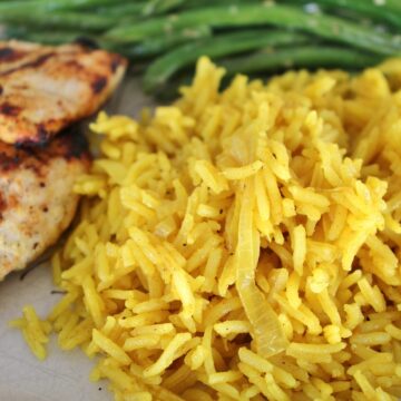 closeup of curried rice pilaf with onions, served with grilled chicken and green beans