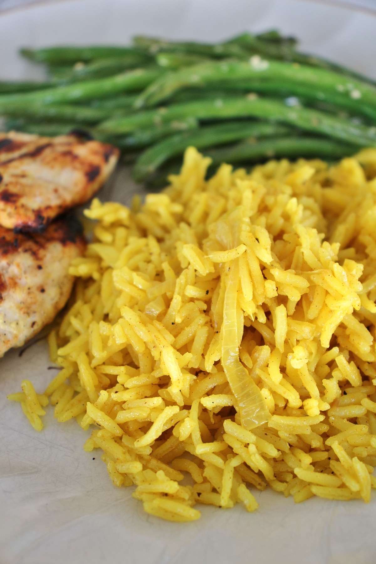 closeup of curried rice pilaf with onions, served with grilled chicken and green beans