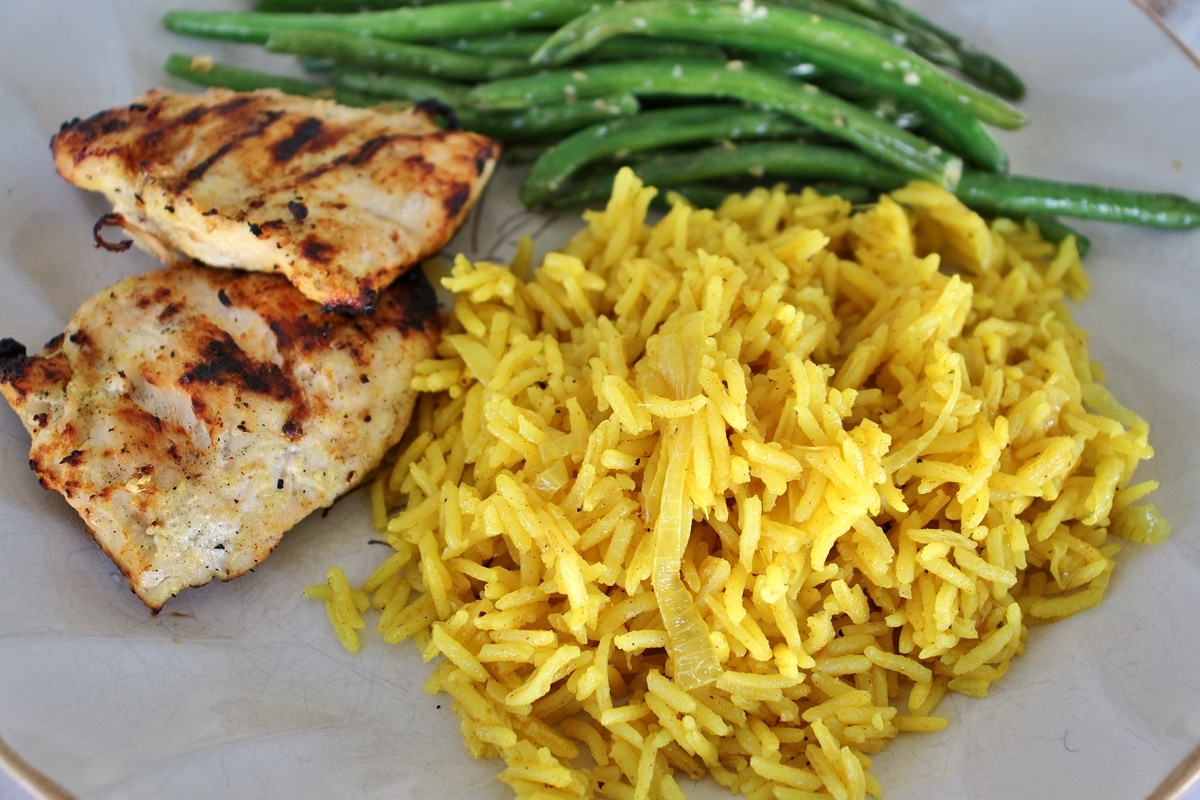 A plate of grilled chicken breast, green beans, and curried citrus rice