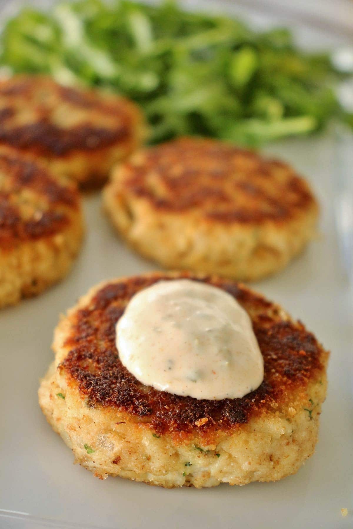 Four golden crab cakes on a white plate with a dollop of sauce on one.