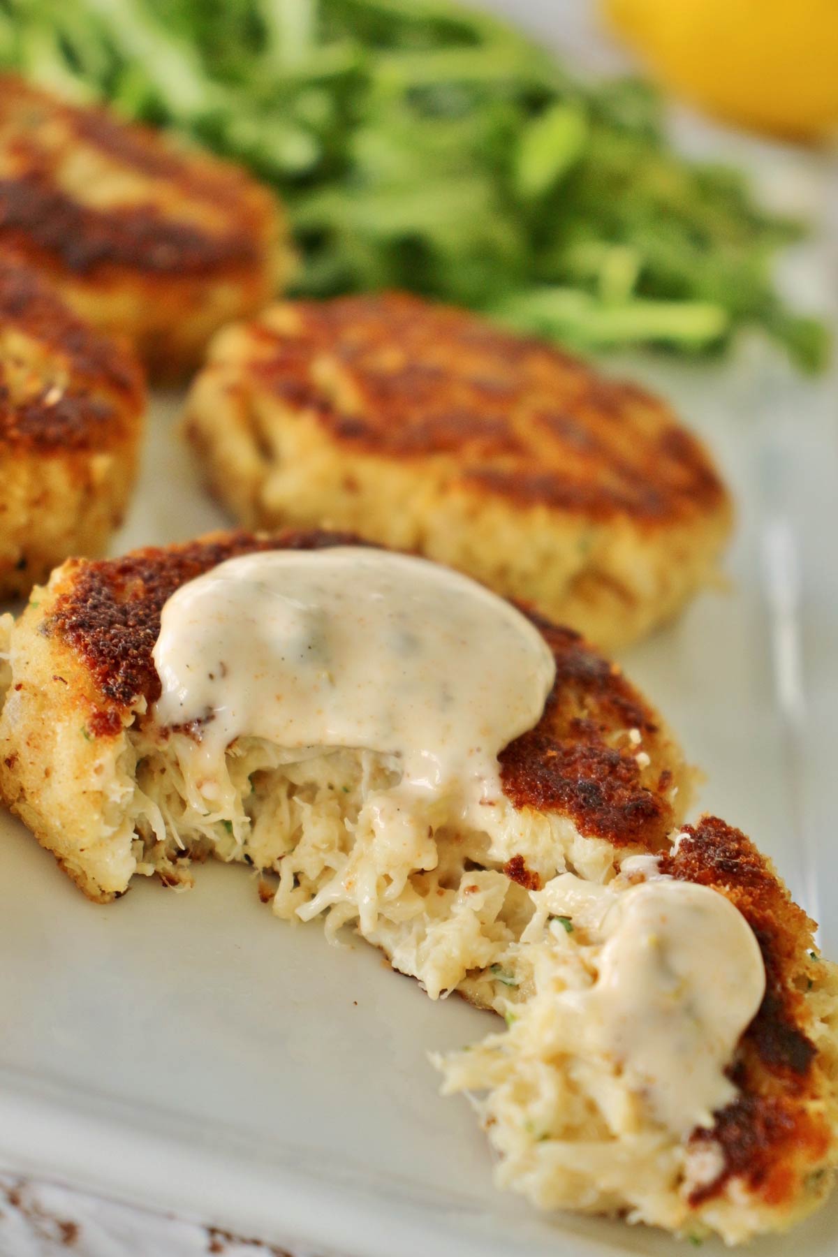 Four golden crab cakes on white plate with a dollop of sauce