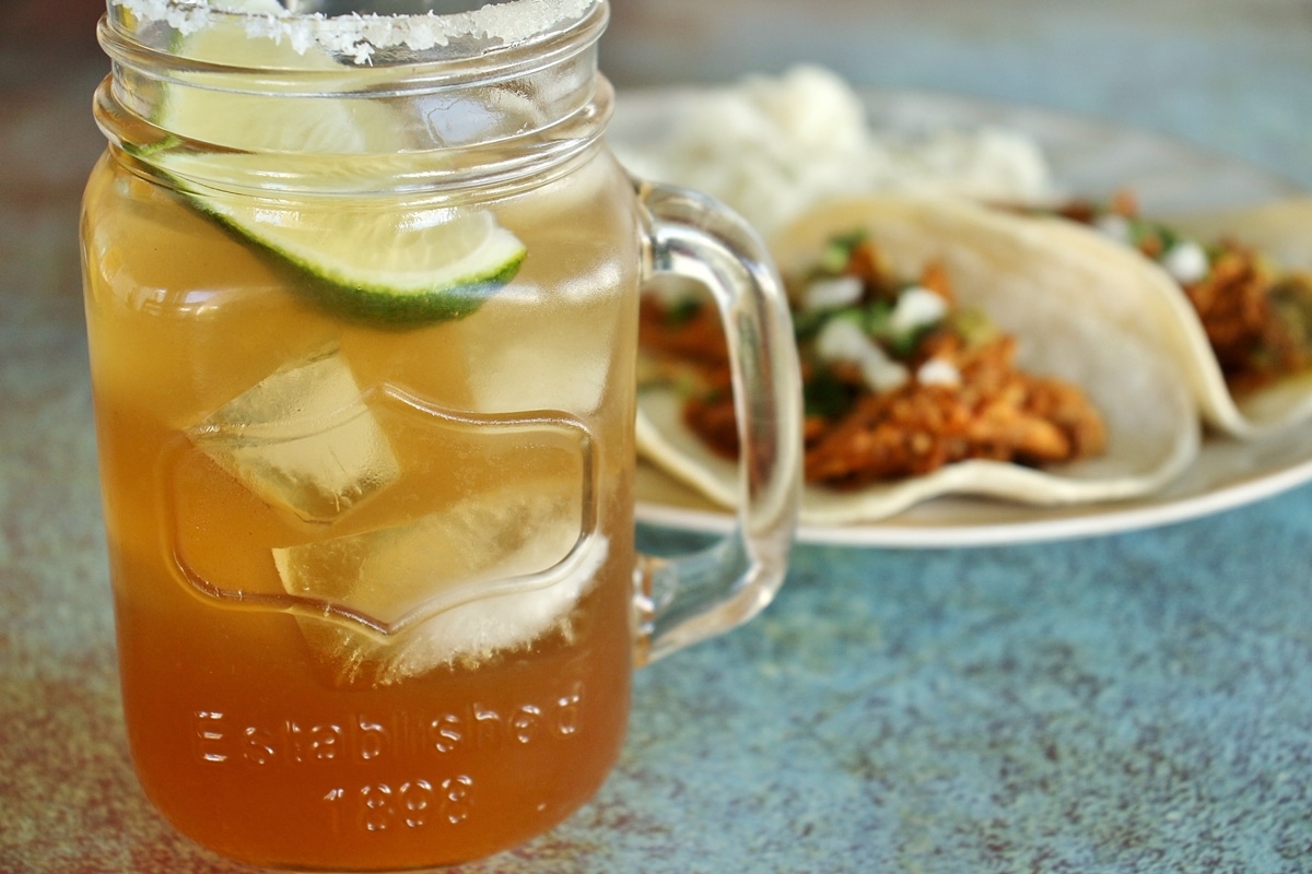 Tamarind margarita in mason jar mug, with plate of tacos in the background