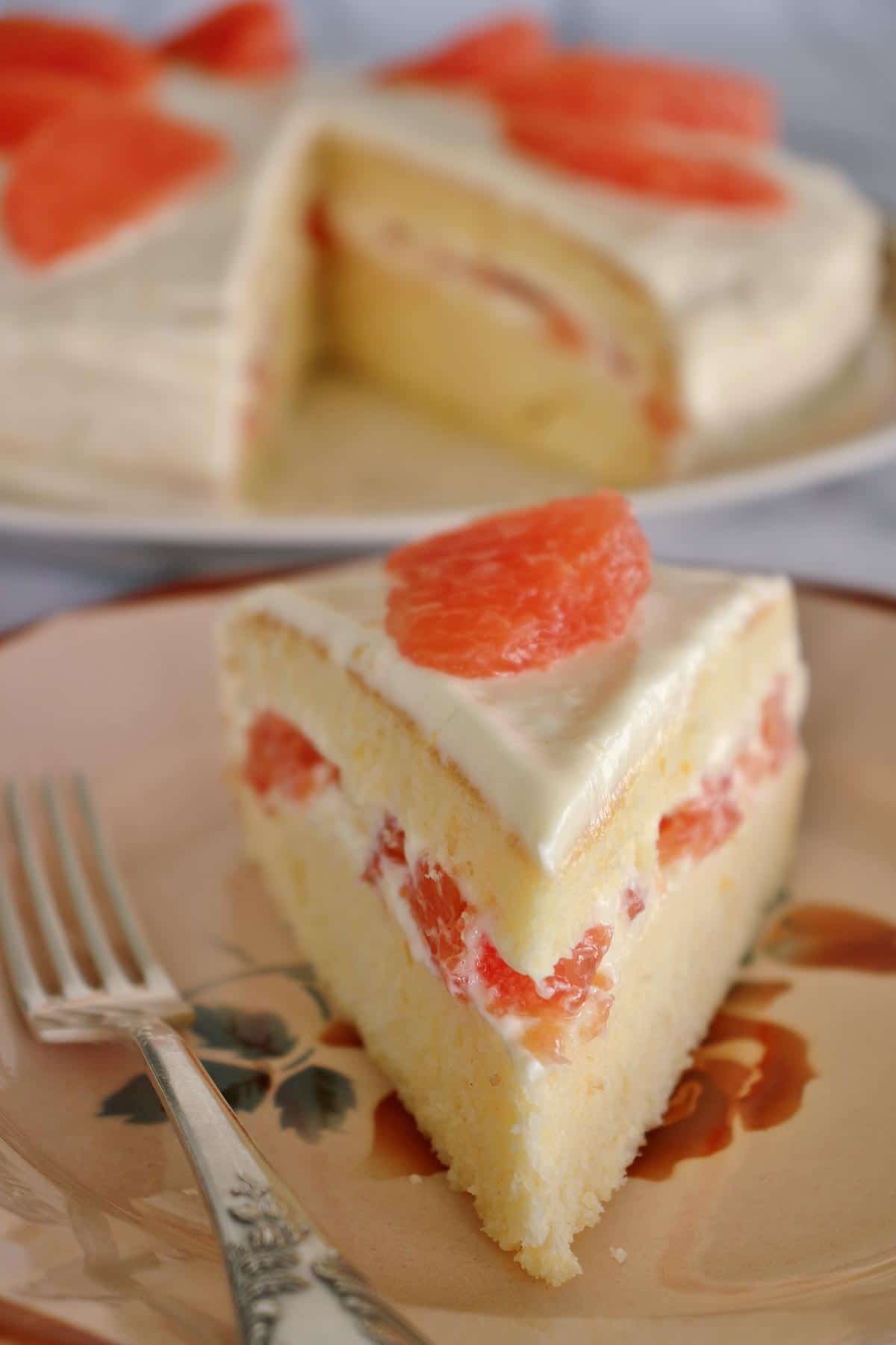 A slice of grapefruit cake on an antique plate with the full cake in the background.