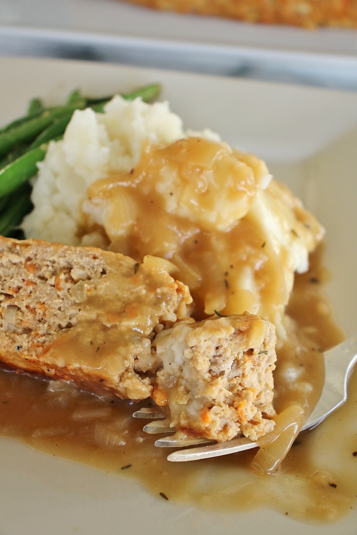 close up of turkey meatloaf, onion gravy, mashed potatoes and green beans