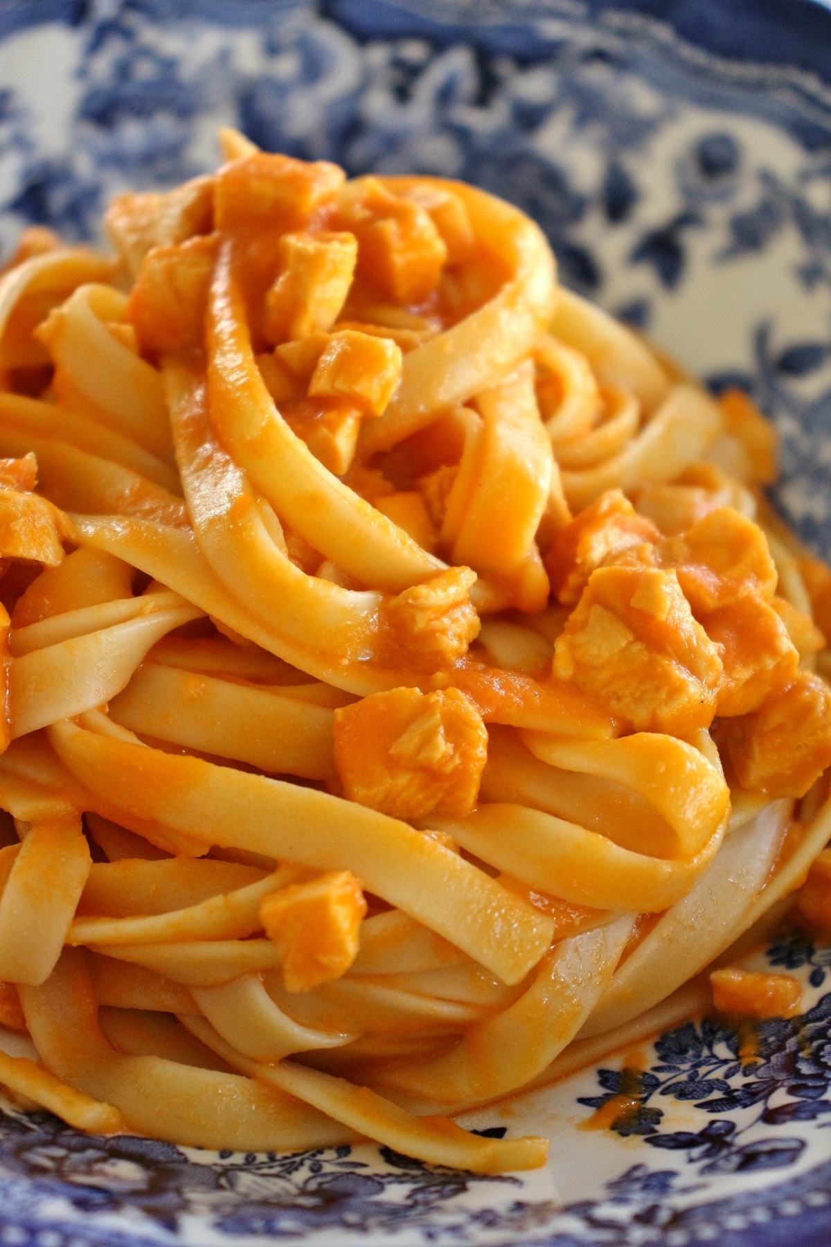 Closeup of fettuccine with bright orange colored Venetian chicken sauce in a blue and white bowl 