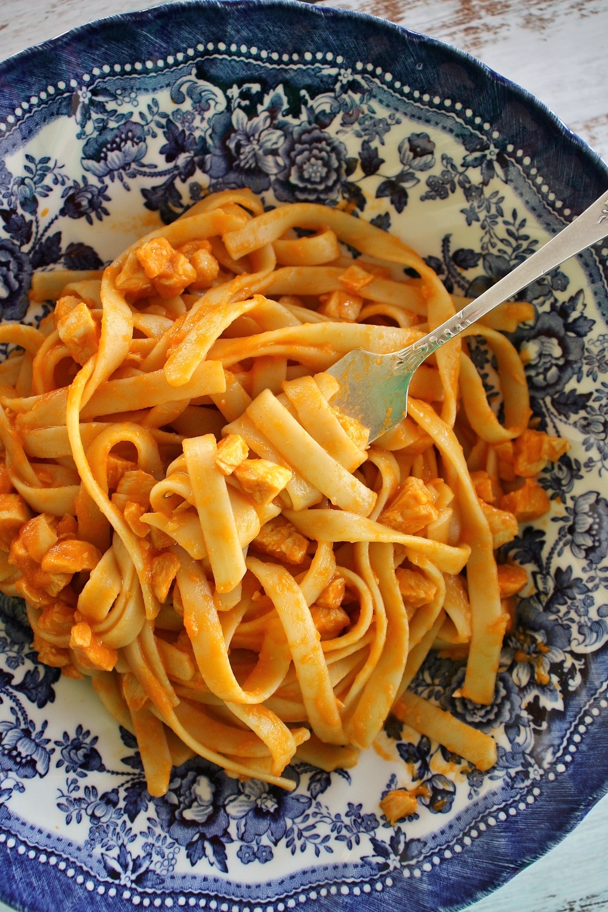 Fettuccine with chicken sauce twirled on a fork in a wide blue and white bowl