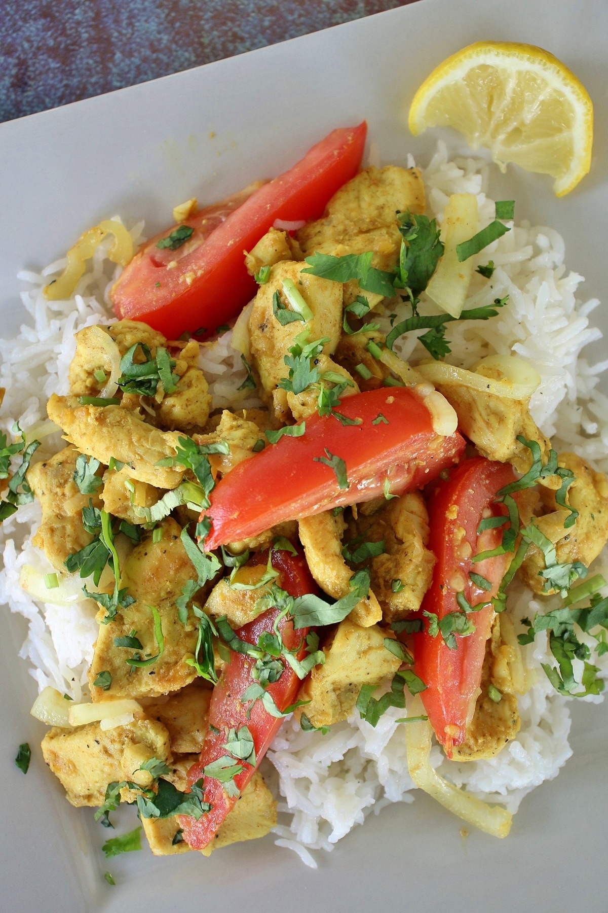 home-style chicken kebat with onions, tomatoes, and cilantro, served over rice on a square plate