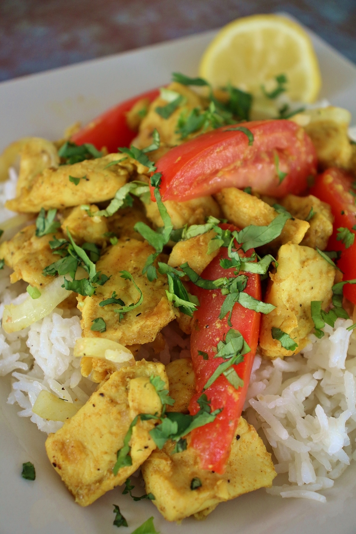 A closeup of home-style chicken kebat with tomato wedges and cilantro garnish served over rice