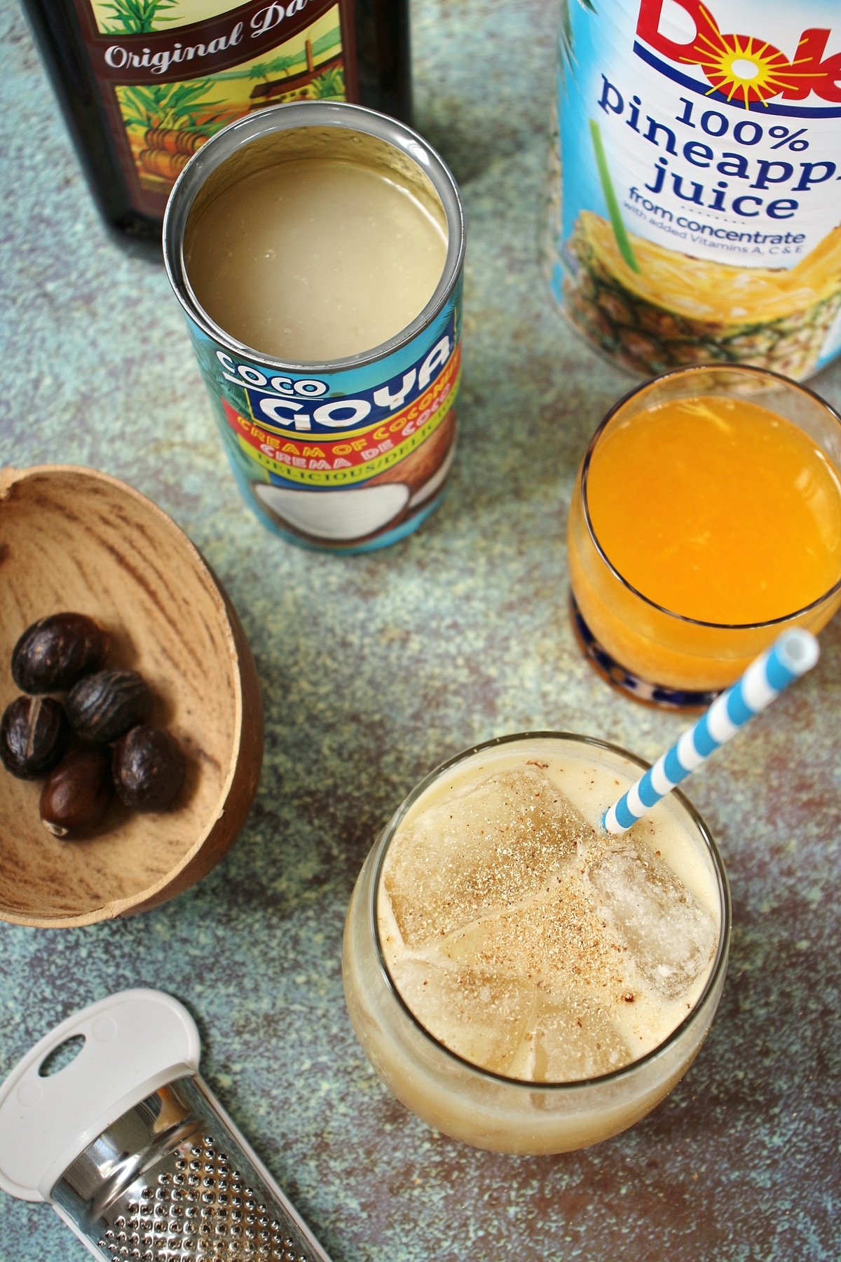 Painkiller cocktail with blue striped straw, cream of coconut, orange juice, pineapple juice, rum