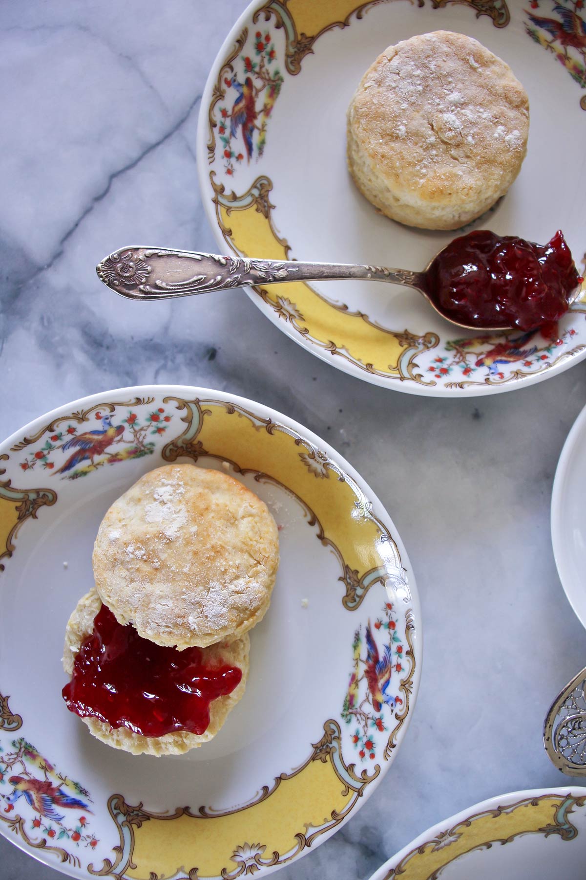 Two dainty afternoon scones served on yellow and white fine china, with strawberry jam