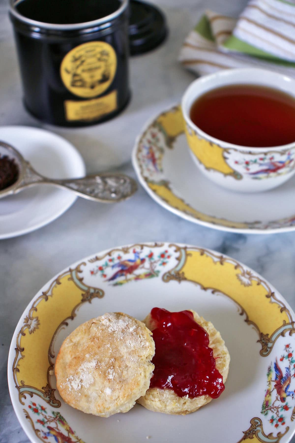 A small British afternoon tea scone topped with strawberry jam, served with a cup of tea in fine china