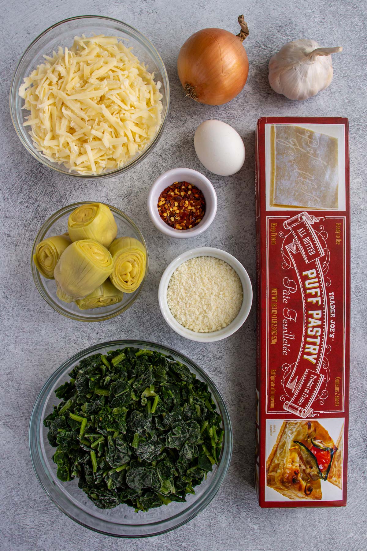 Ingredients for spinach and artichoke puff pastry swirls on a light grey background.