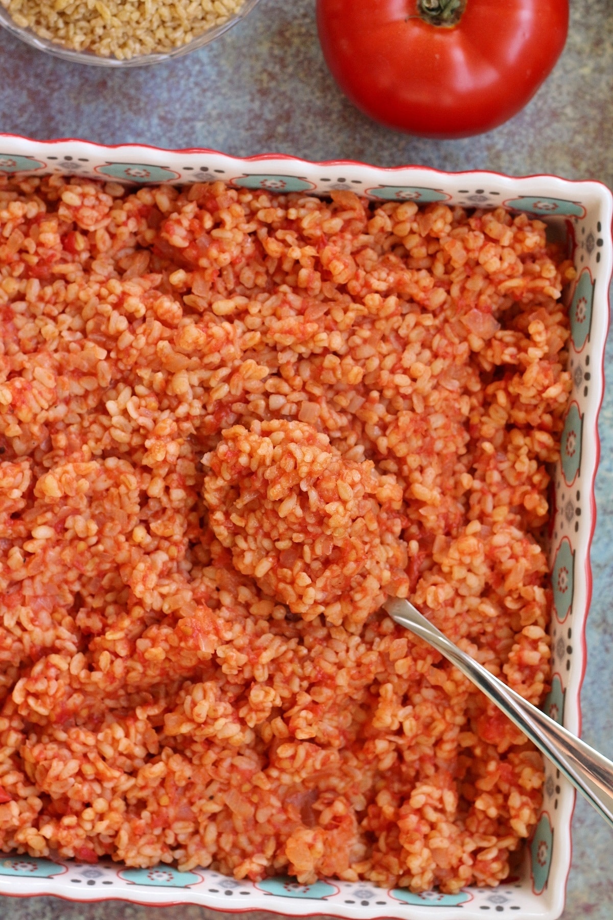 overhead view of a colorful square baking dish filled with tomato bulgur pilaf