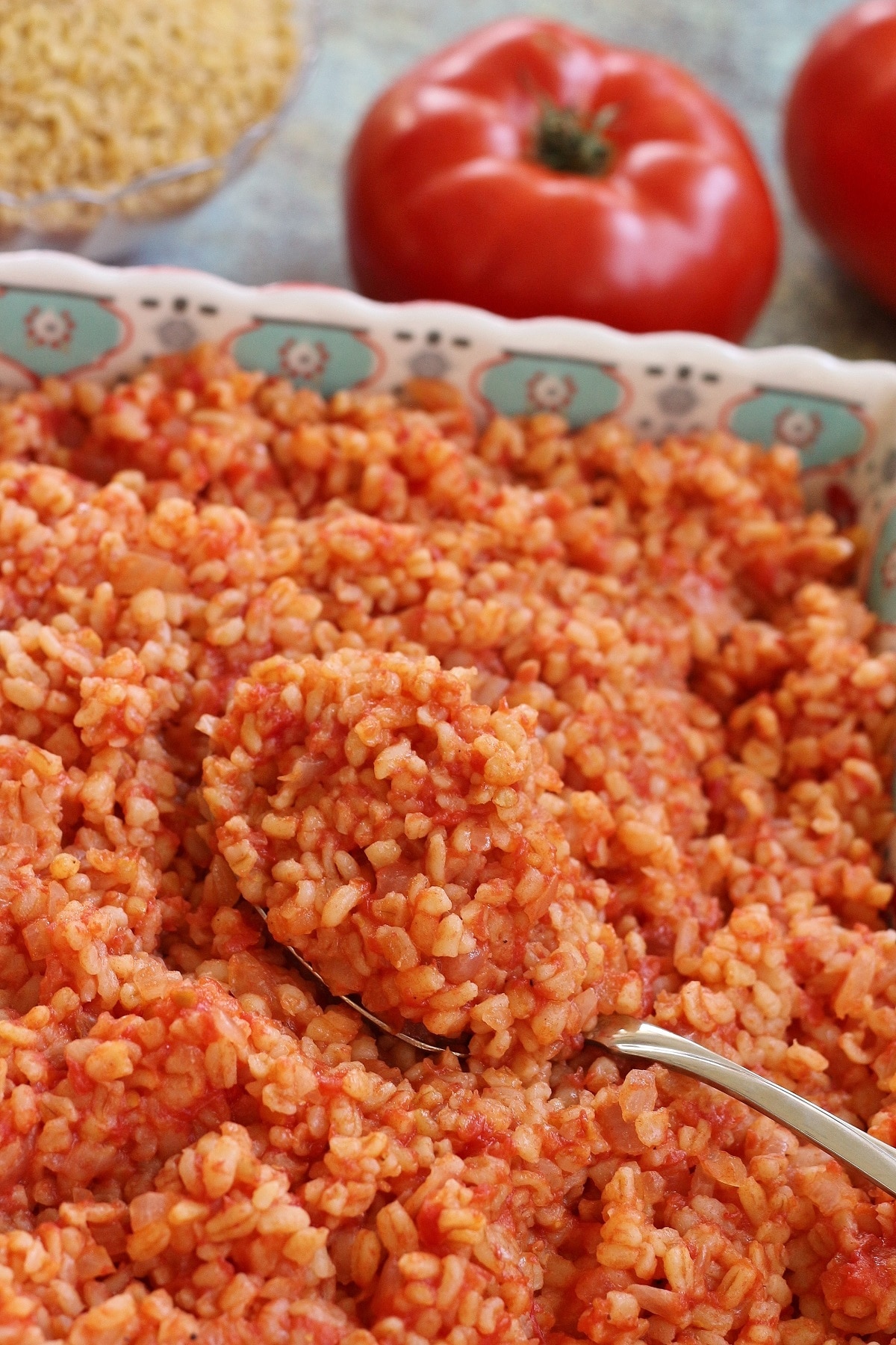 closeup of a big scoop of tomato bulgur pilaf in a square serving dish