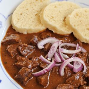 closeup of Czech beef goulash and dumplings with red onions on top