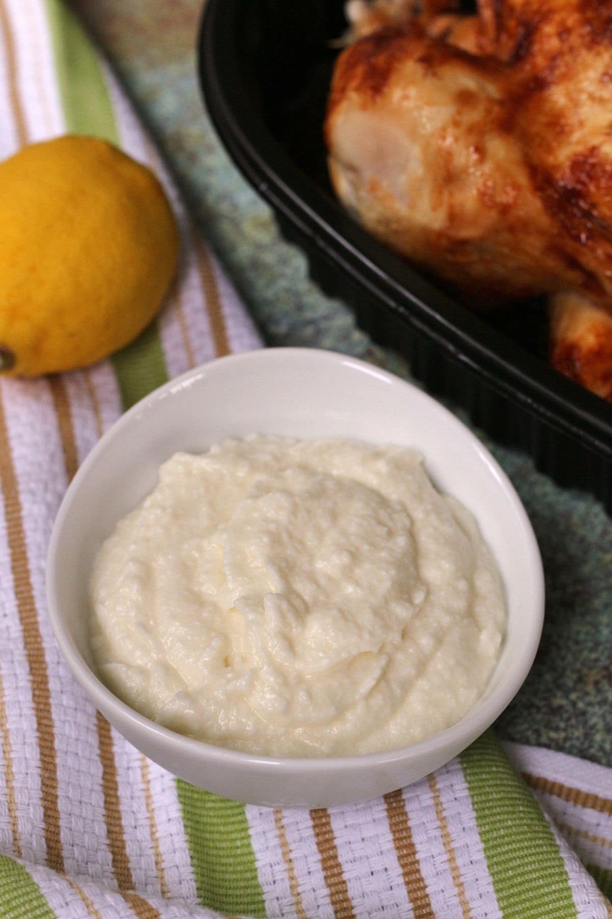 creamy Armenian garlic sauce in a white bowl with lemon and chicken in the background