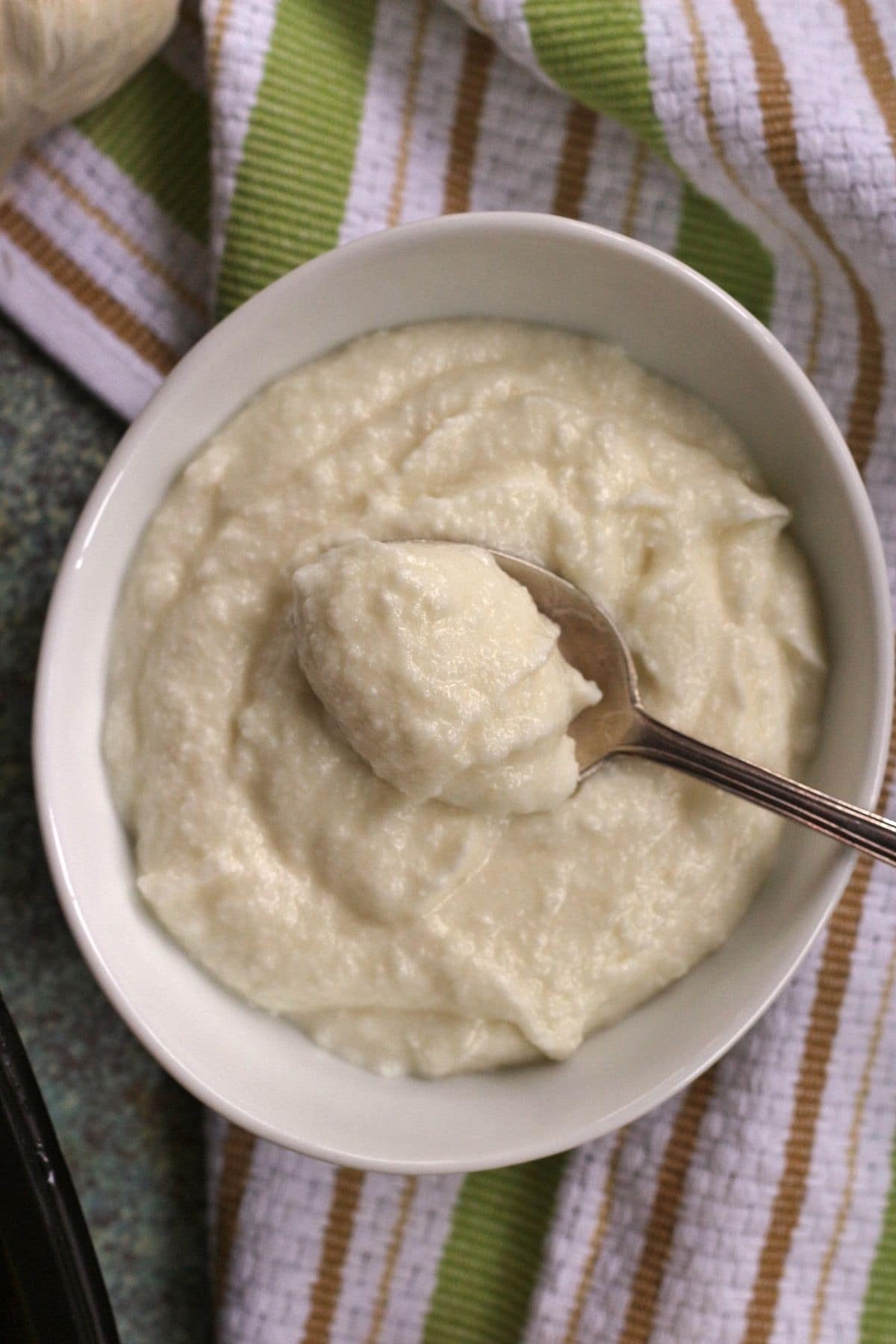 overhead closeup of creamy white garlic sauce in a white bowl with a spoon