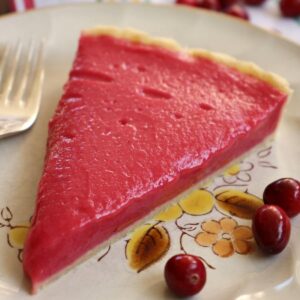 Closeup of a slice of cranberry curd tart on a plate with 3 cranberries.
