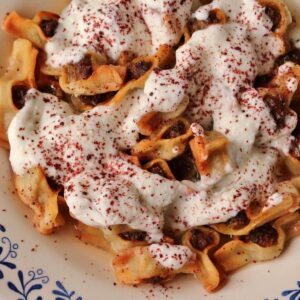 A shallow bowl filled with canoe-shaped meat-filled dumplings topped with yogurt sauce.