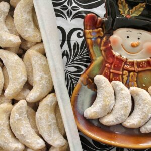 A cookie tin and snowman plate filled with vanilla crescent cookies.