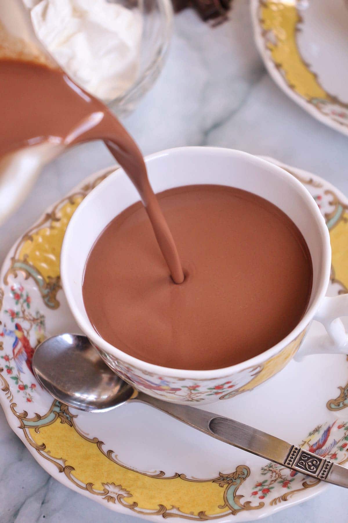 Closeup of French hot chocolate pouring from a pitcher into a ceramic cup.