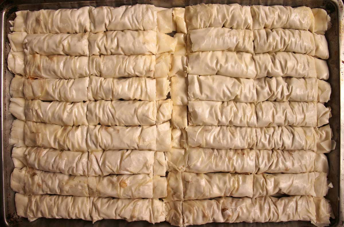 A baking sheet of unbaked rolled baklava brushed with butter and cut into pieces.