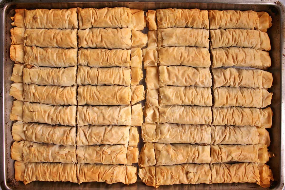 A baking sheet of baked rolled baklava before adding the syrup.