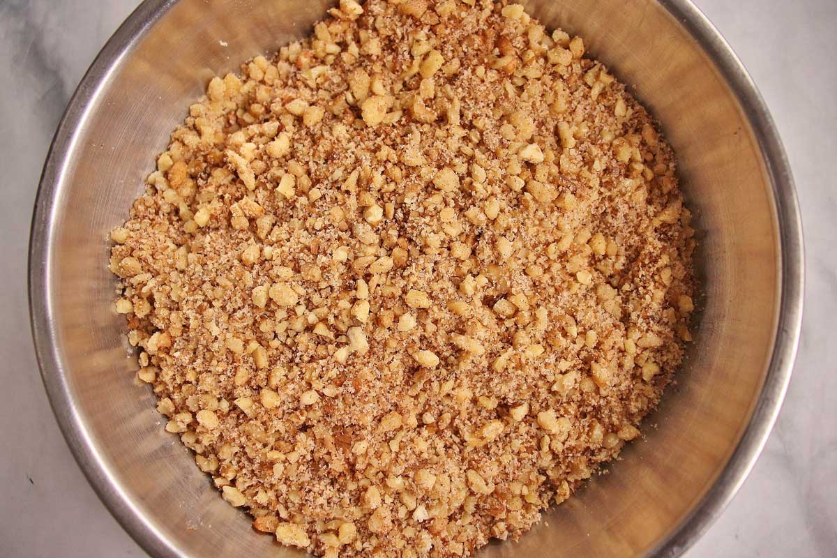 A mixture of chopped walnuts with cinnamon and sugar in a metal mixing bowl.