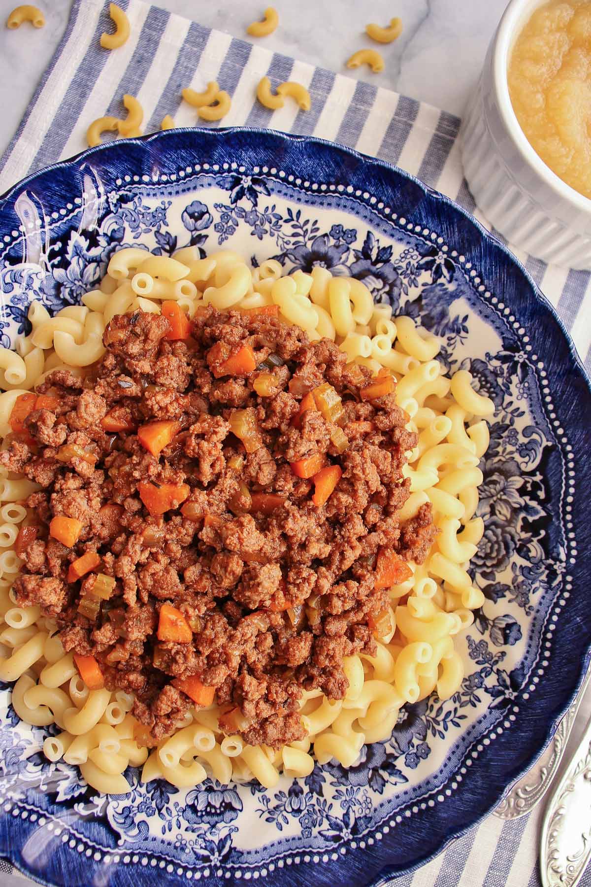Closeup of macaroni topped with meat sauce in a shallow blue and white bowl.