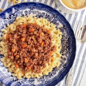 A shallow blue and white bowl filled with elbow macaroni and meat sauce.