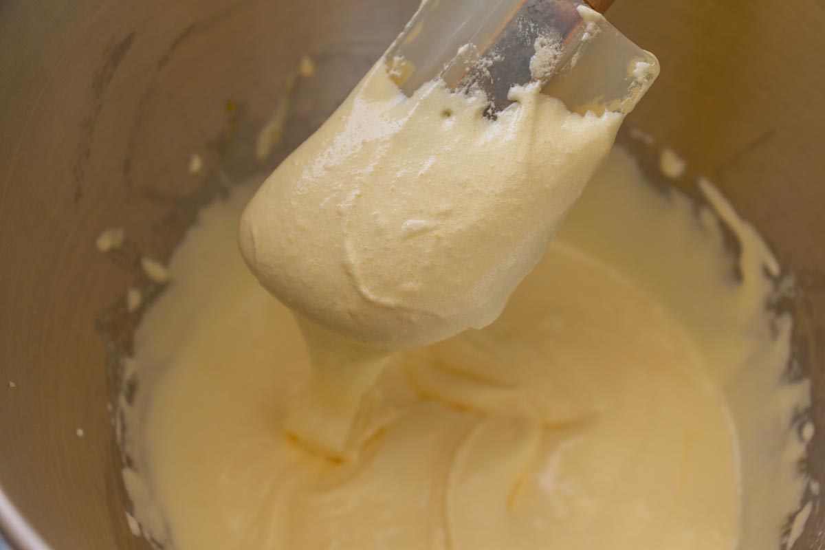 A rubber spatula lifting a creamed mixture of egg yolks and sugar out of a bowl.