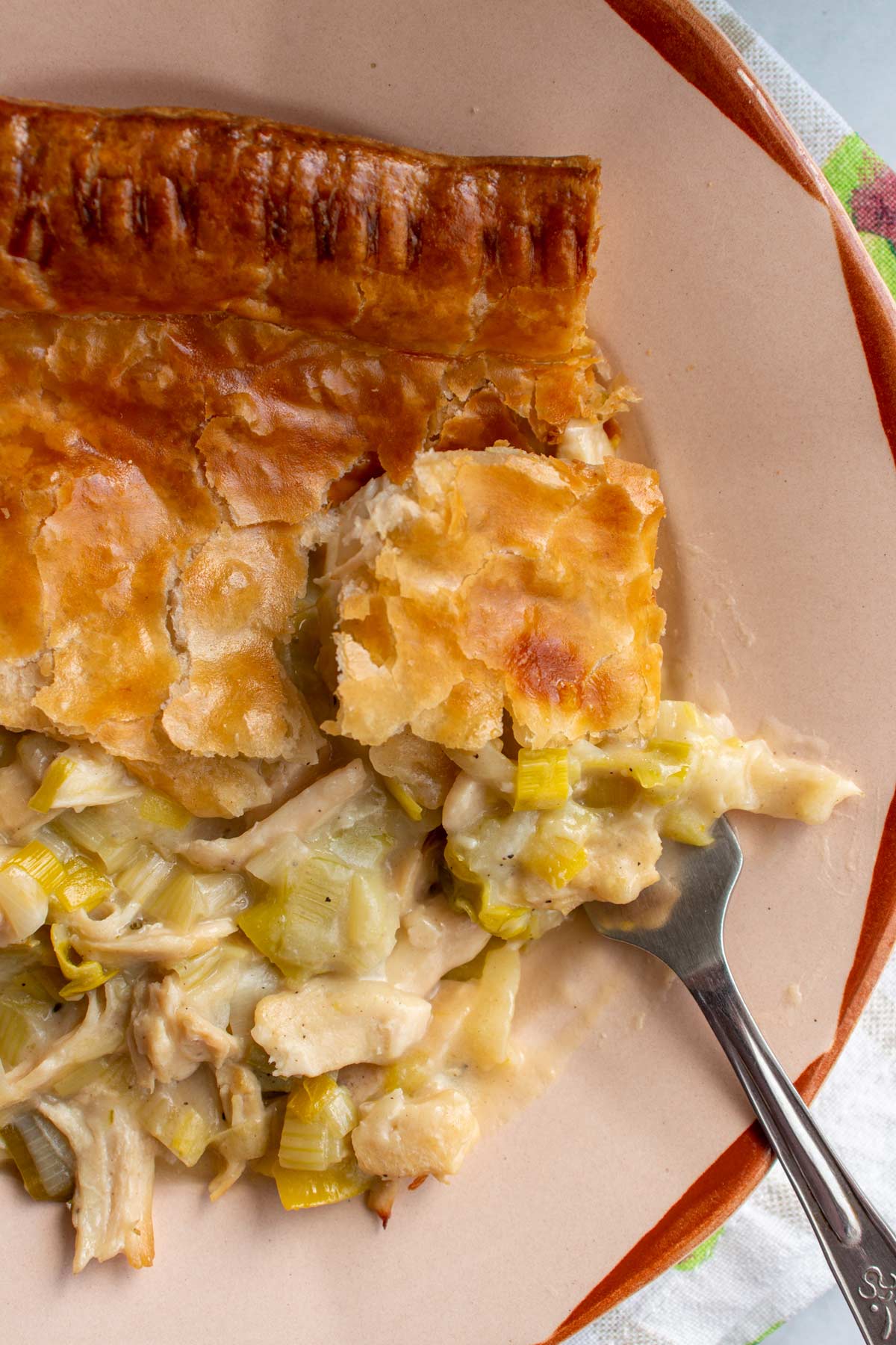 Closeup of chicken and leek pie on a rustic plate with a fork scooping some up.